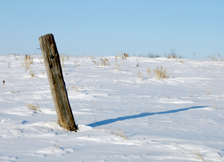 Old leaning fencepost in snow