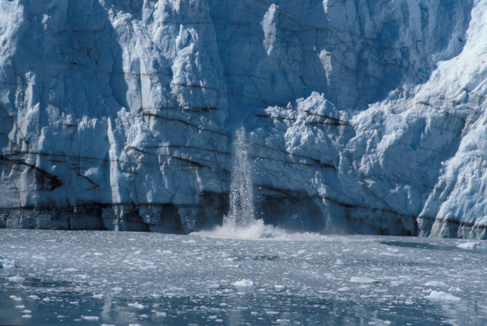 Ice splashes from black-streaked glacier into Alaskan waters