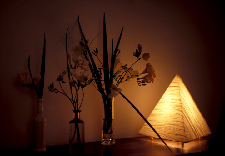 A tetrahedron-shaped lamp and flower arrangements on a dark wood surface