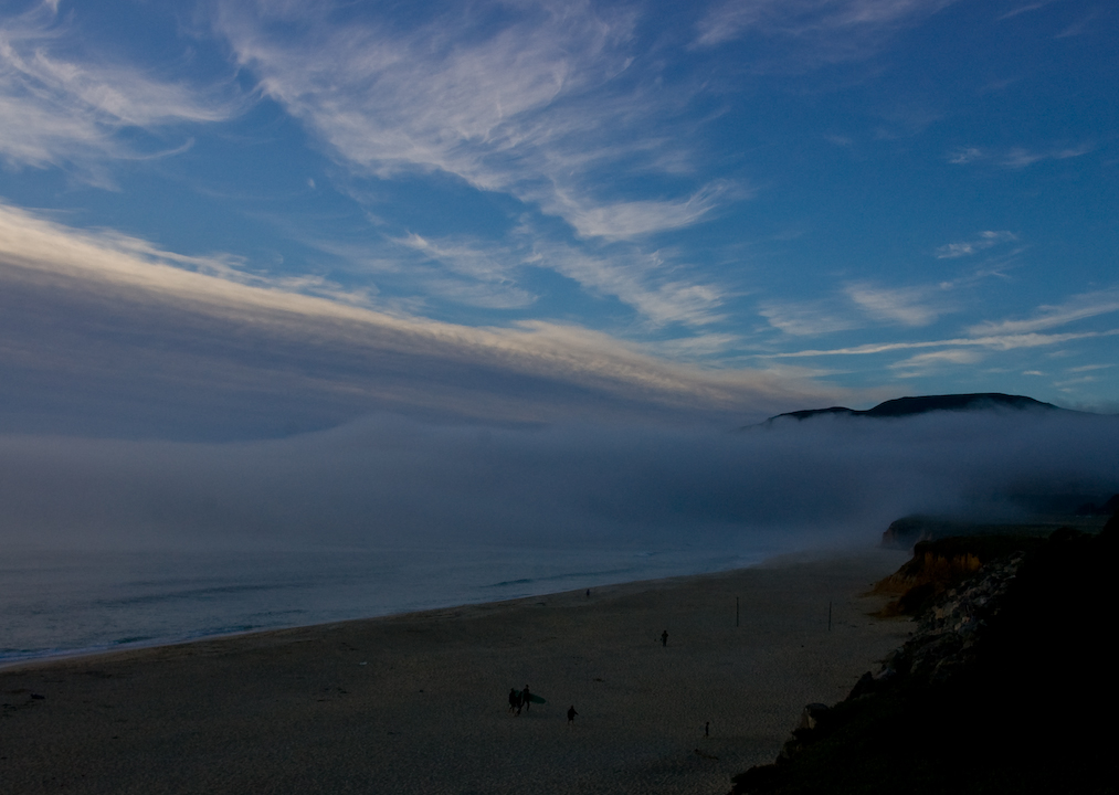 Northern California beach at dusk, with returning surfers