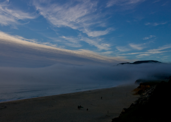 Northern California beach at dusk, with returning surfers