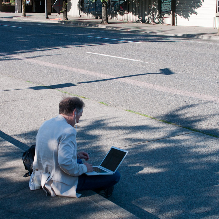 Man sitting on curb with laptop
