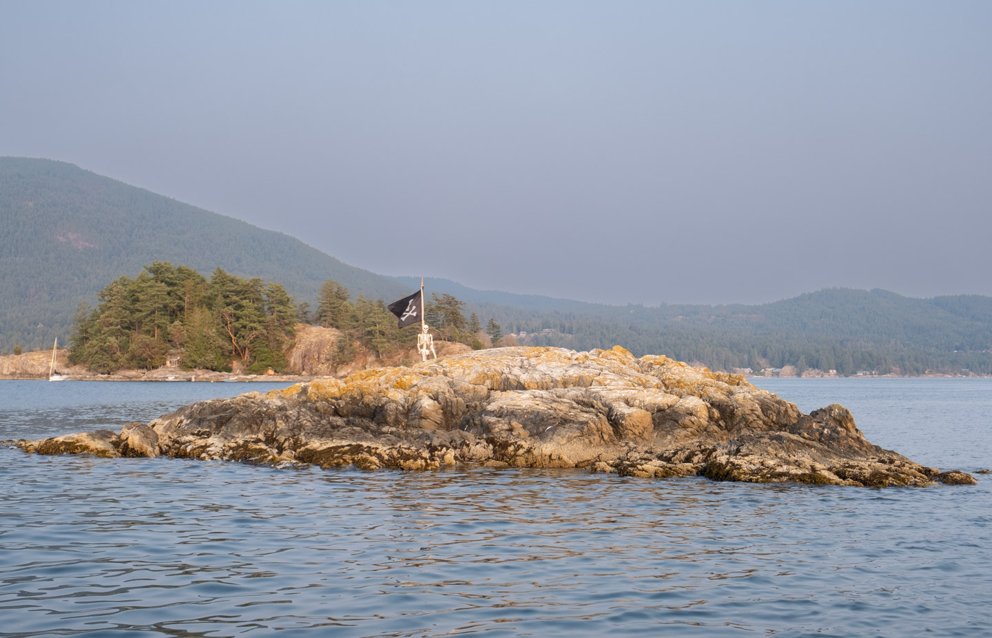 Small rocky island in Átl’ḵa7tsem decorated with a skeleton and Jolly Roger