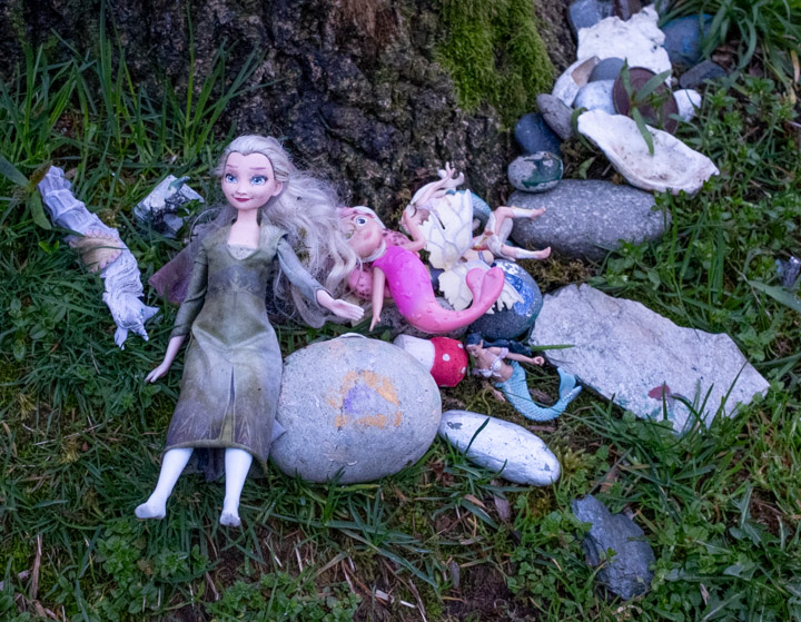 Dolls and related tree artifacts at the base of a tree in dim light