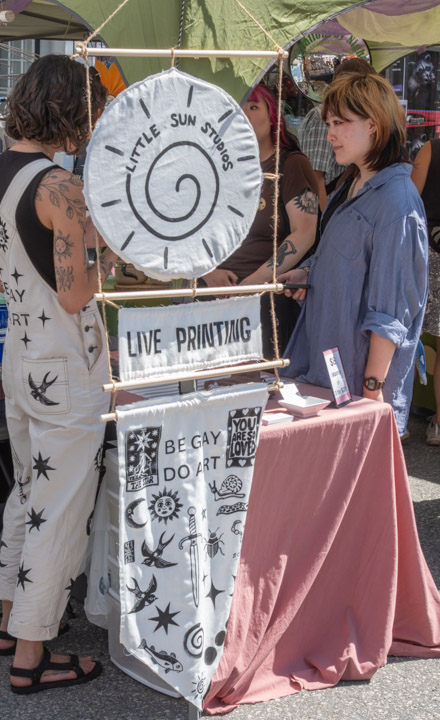 Little Sun Studios live printing has a banner saying “BE GAY DO ART
