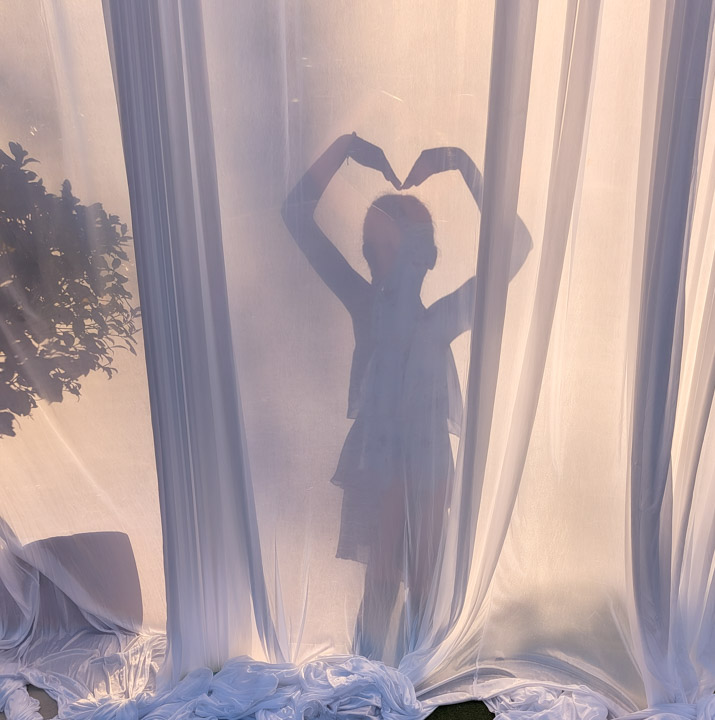 A young girl silhouetted making a heart with her arms