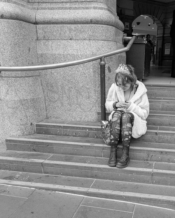 A young woman looks at her phone seated on a stone staircase